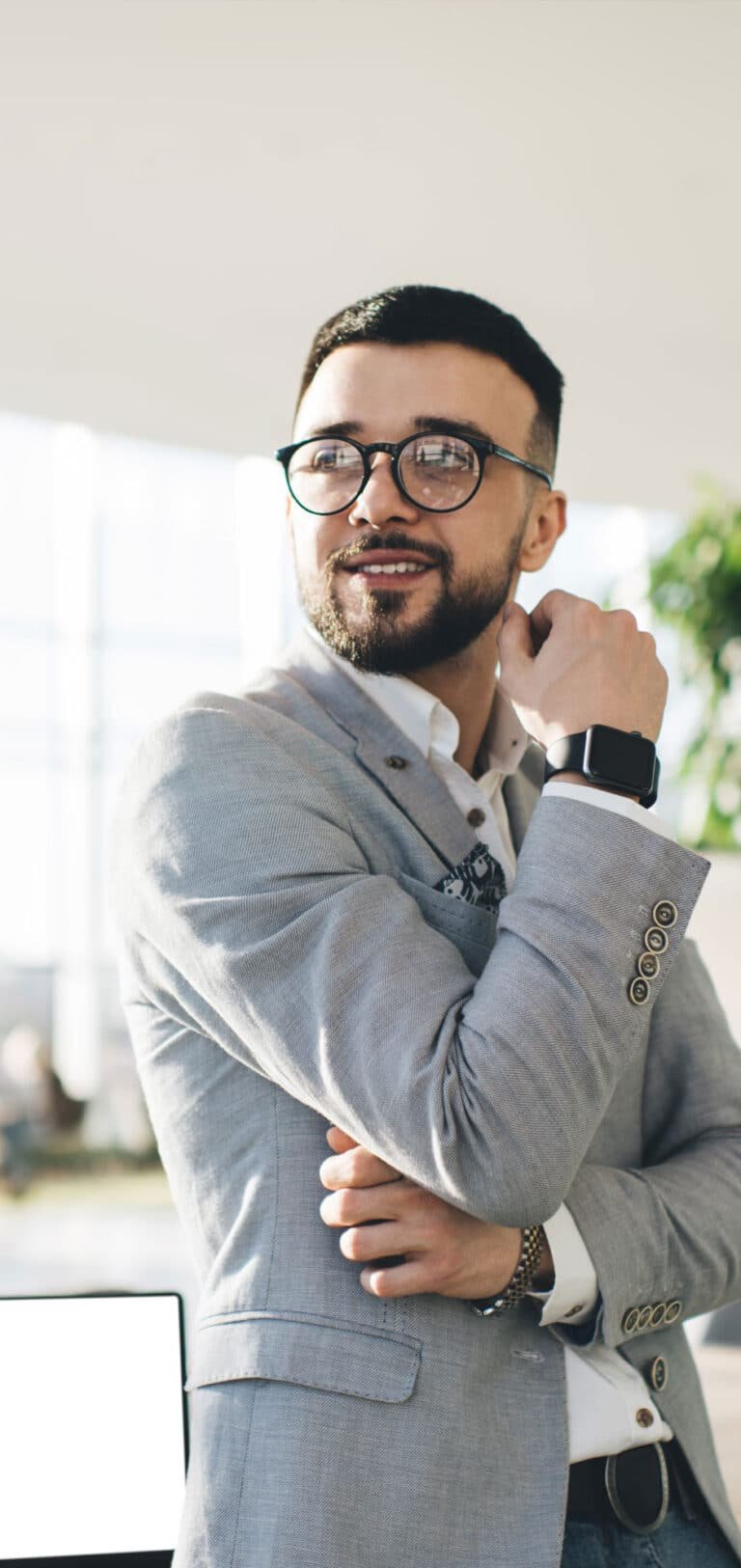 Homem branco de oculos e vestindo sueter encostado na mesa de trabalho